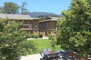 Exterior of building viewed between trees, with outdoor seating area with mountains in distance