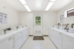 Interior Laundry room, multiple Washers & Dryers, white appliances, white walls, tile floor.