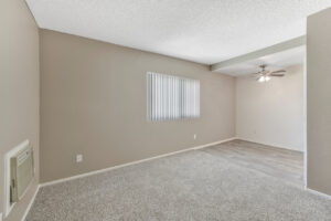 Interior Unit Living Room, window along left wall, ceiling fan/lights in dining area, neutral toned wall paint and carpeting.