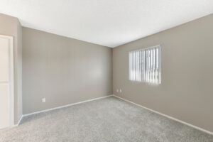 Interior Unit Bedroom, neutral toned wall paint, neutral toned carpeting, accordian blinds, window on far side wall